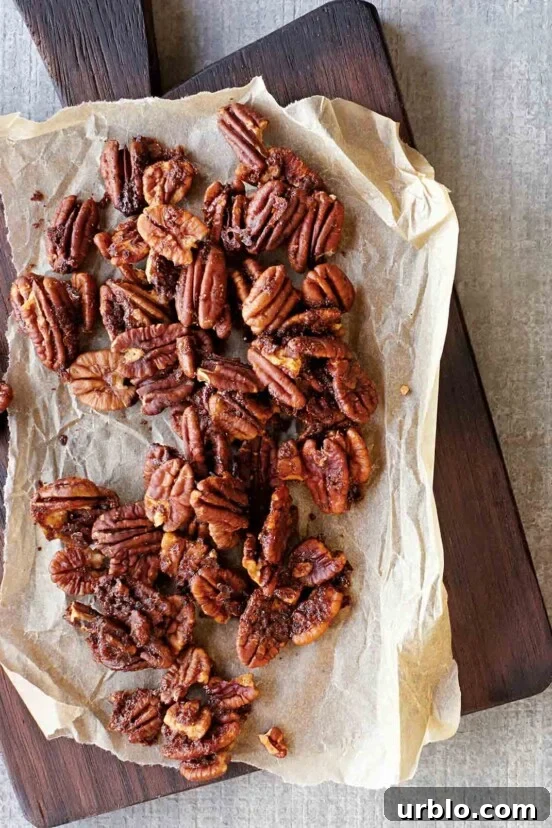 Baked spiced pecans on a sheet of parchment that is resting on a wooden serving board.