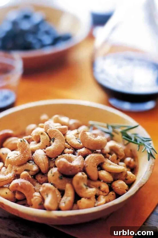A bowl filled with Ina Garten's rosemary cashews with a sprig of rosemary on the side.