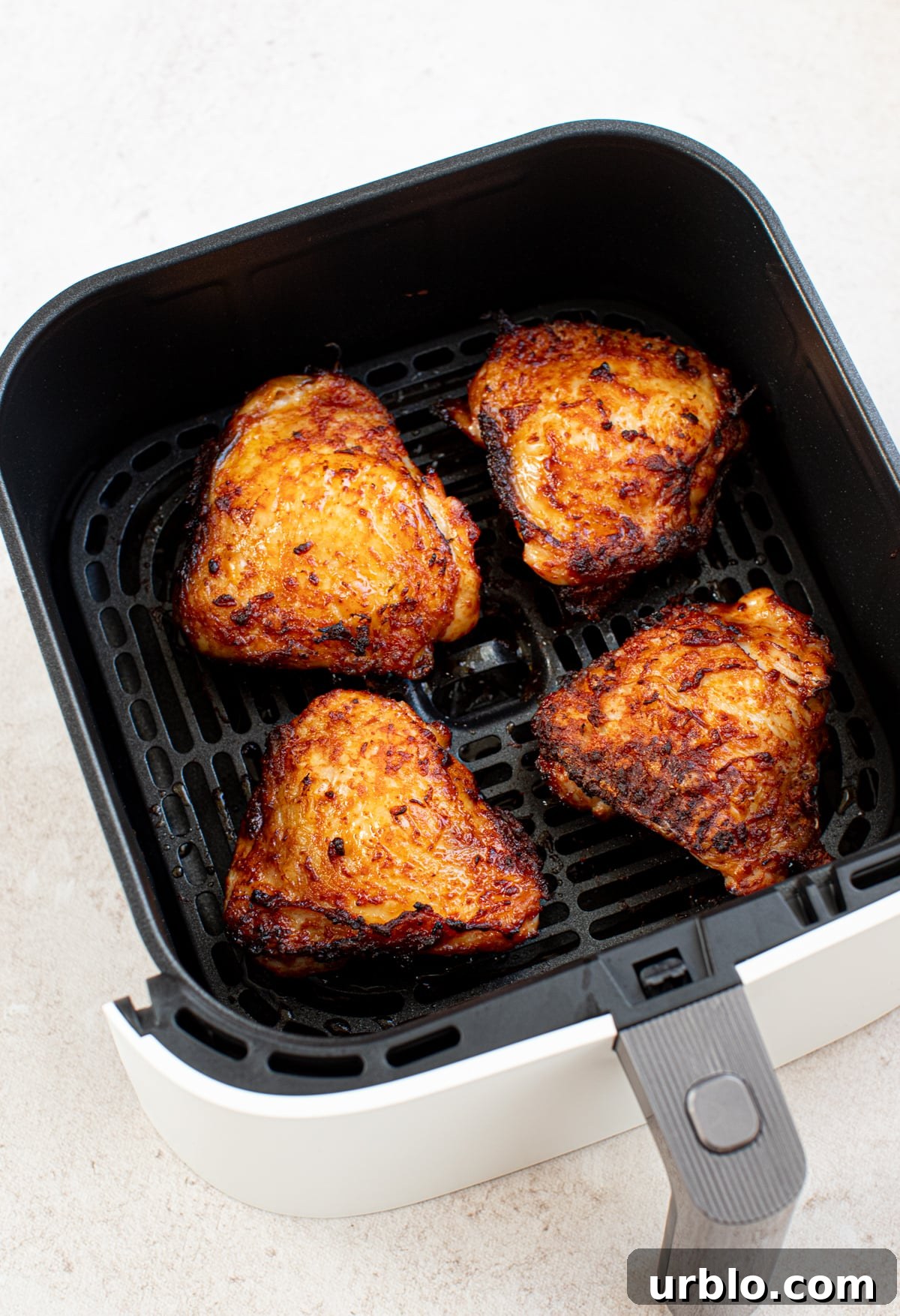 Four juicy air fryer chicken thighs in a fryer basket after cooking. 