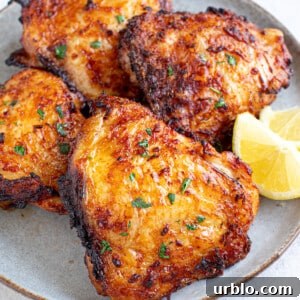 Four easy air fryer chicken thighs sit on a plate with lemon wedges on the side.