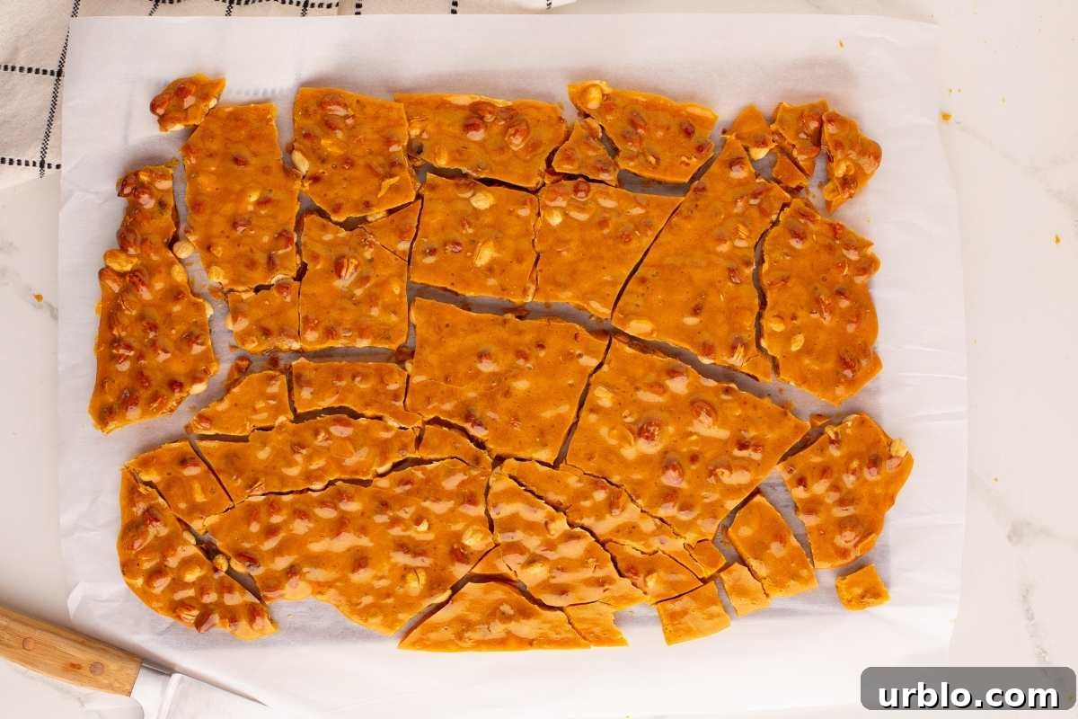 Classic Old-Fashioned Peanut Brittle Recipe 8 Broken peanut brittle pieces on parchment paper with a knife.