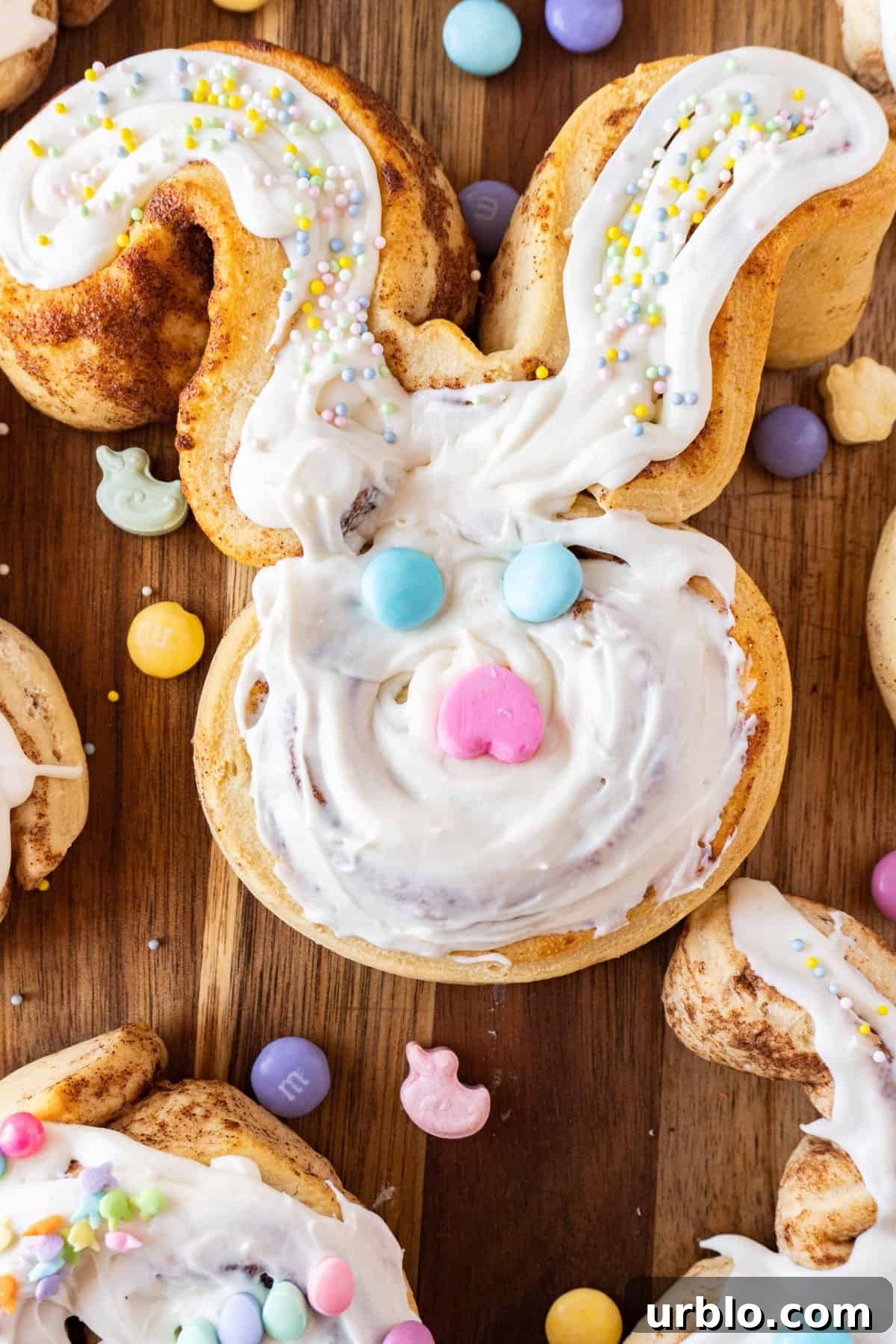 large bunny cinnamon roll on a cutting board with Easter candies sprinkled around it.