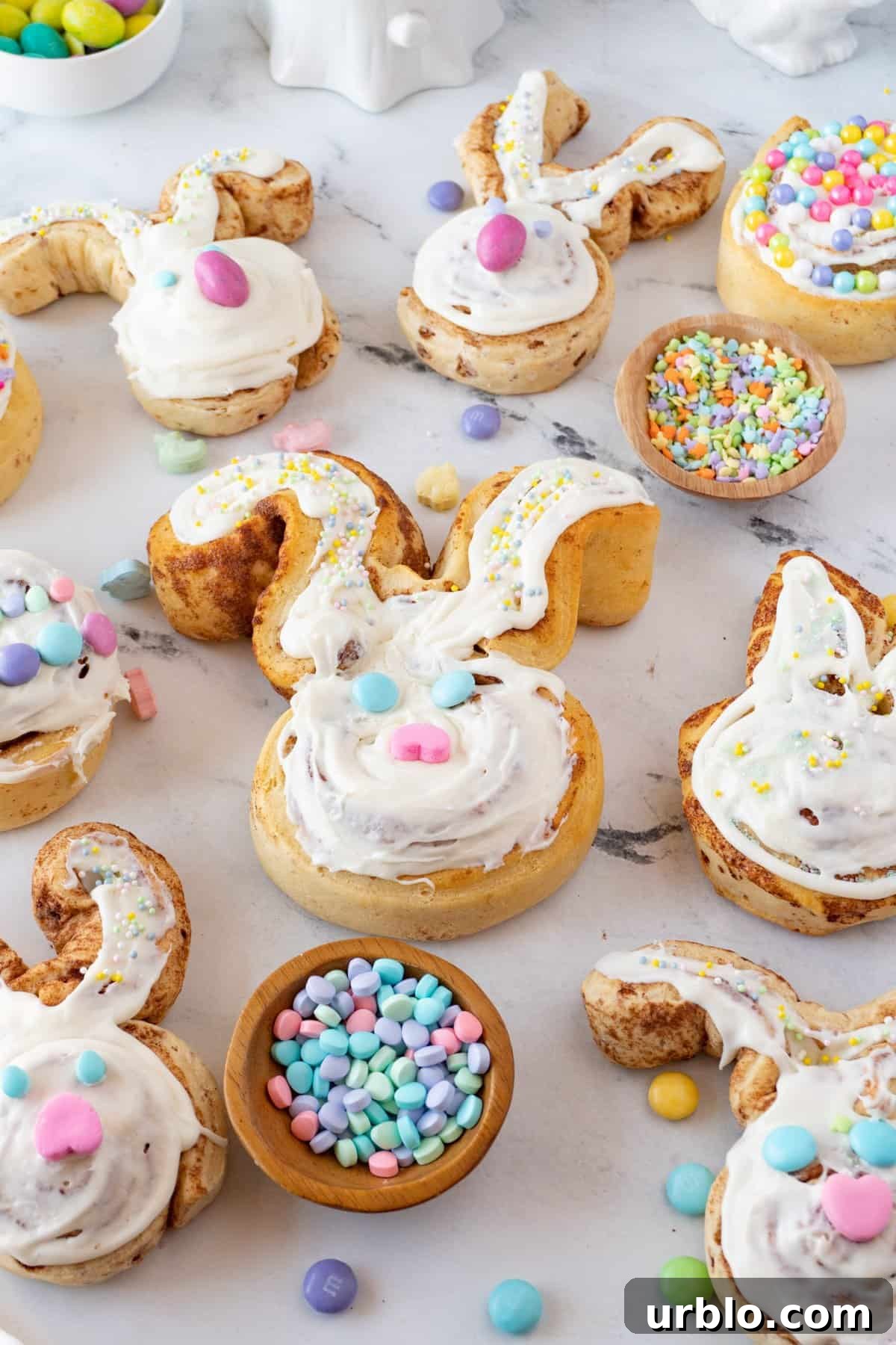 bunny cinnamon rolls on marble background with Easter candies and sprinkles used to decorate them.