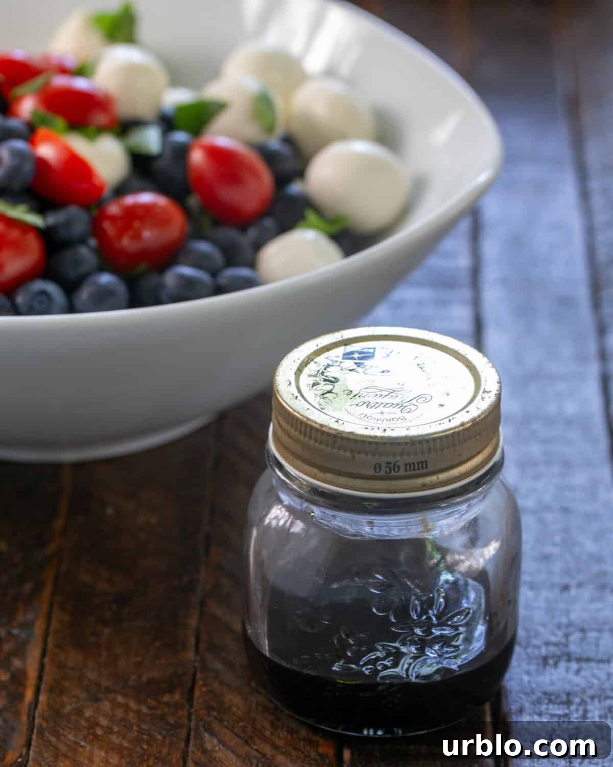 Blueberry Caprese Salad in a white bowl with Balsamic vinegar.