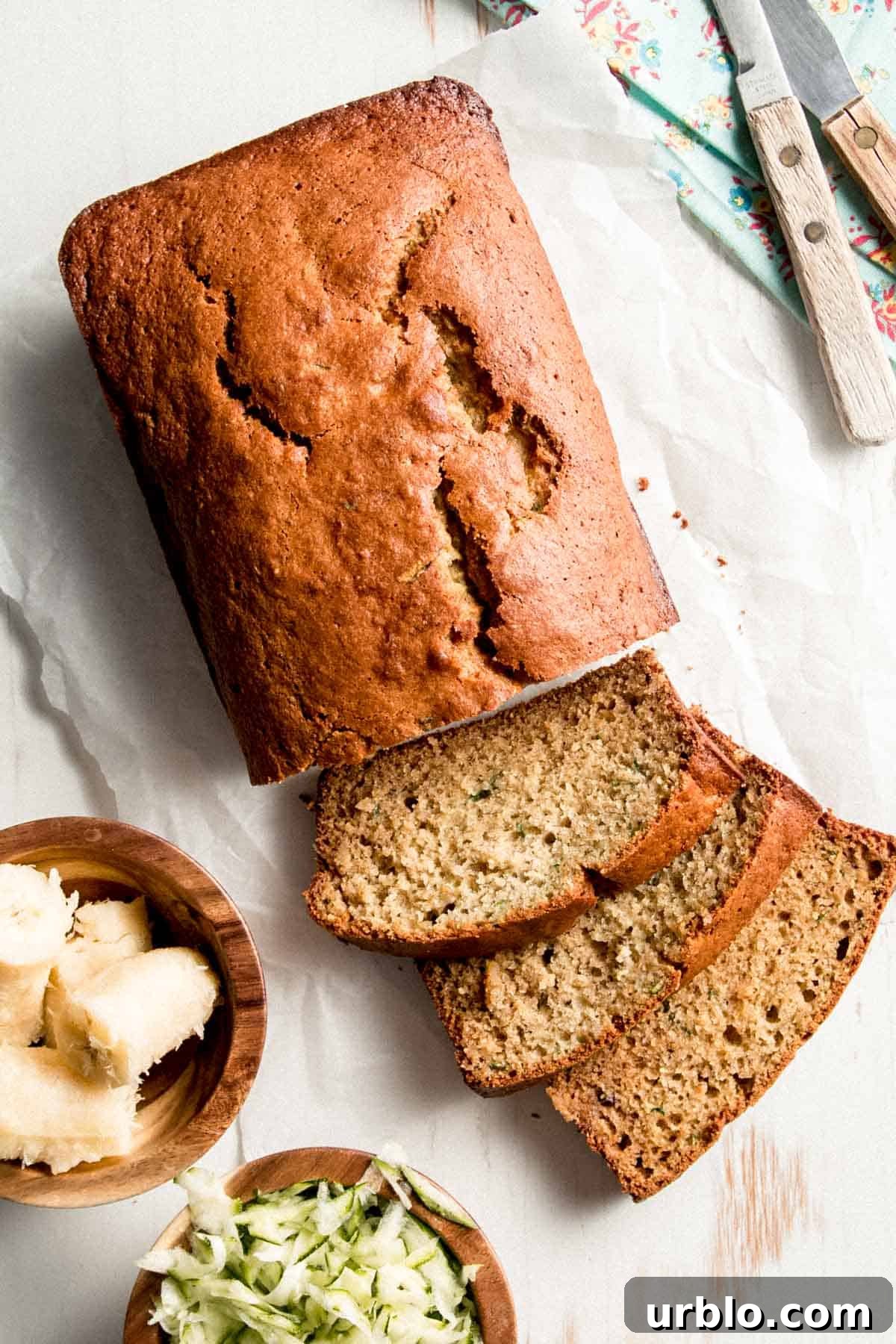 A loaf of Gluten-free Zucchini Banana Bread with a few slices laid on their sides next to small bowls of ripe banana and grated zucchini.