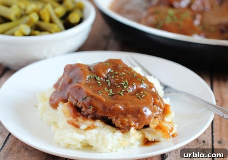 salisbury steak on a plate with pan and veggie behind it