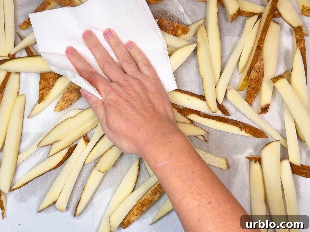 Hand using a paper towel to blot excess moisture from cut potatoes after they have soaked in water.