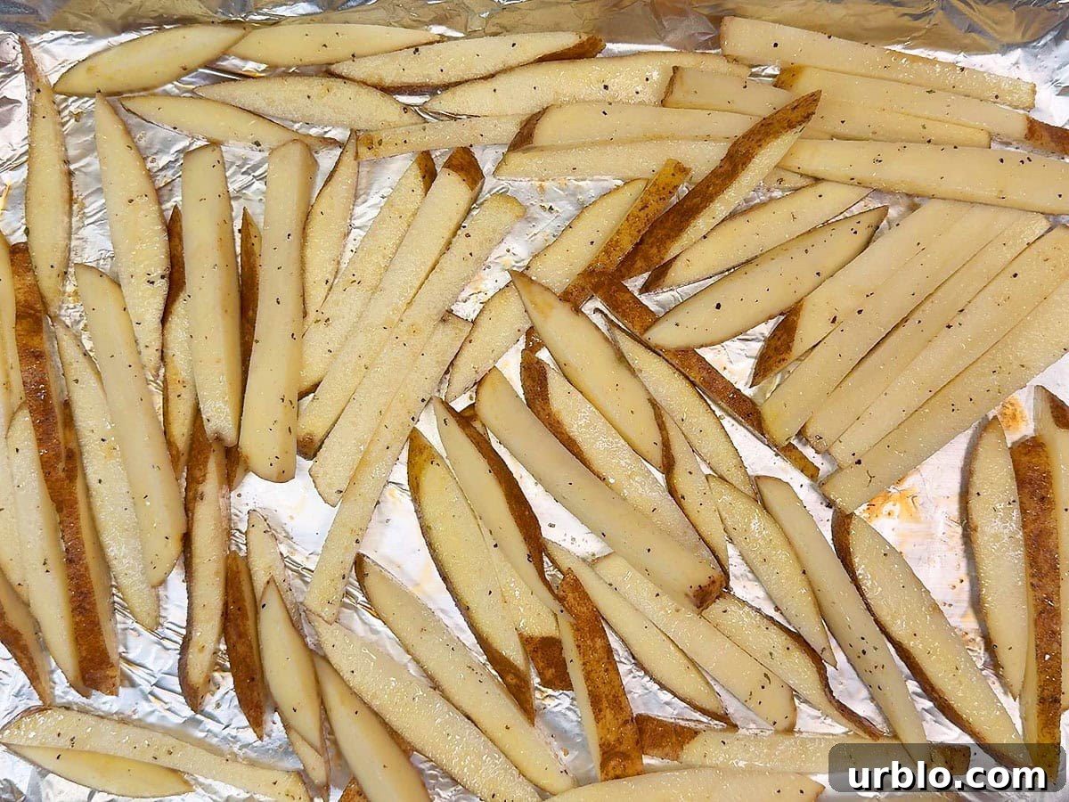 Seasoned cut potatoes on a foil lined and greased baking sheet.