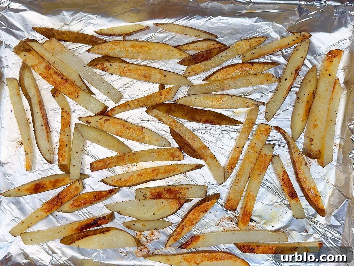 Cooked oven baked French fries on a foiled lined and greased cookie sheet.