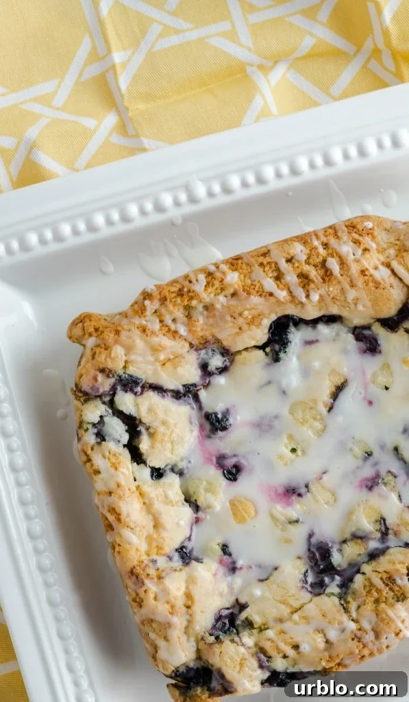 Glazed blueberry lemon bars uncut on white square dish. 