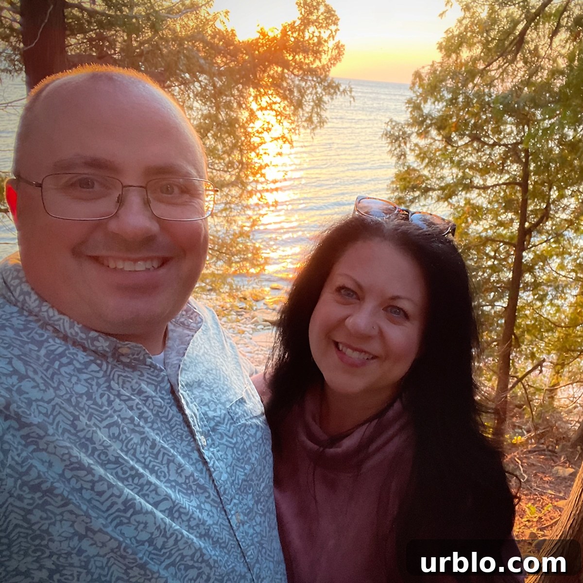 Steve and Rebecca Blackwell standing on the coast of Door County with the sun setting over the water behind them.