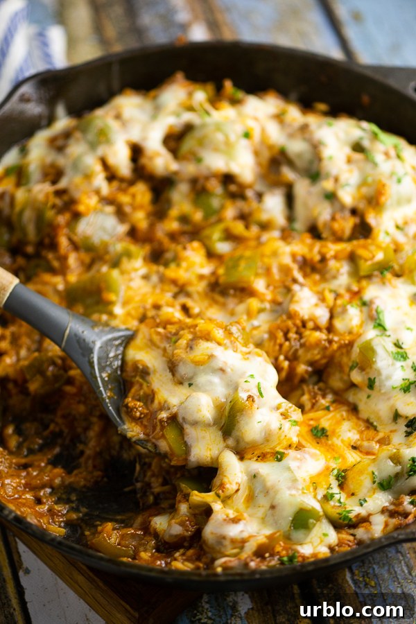 Unstuffed peppers covered in melted mozzarella in a cast iron skillet with a spoon in the middle