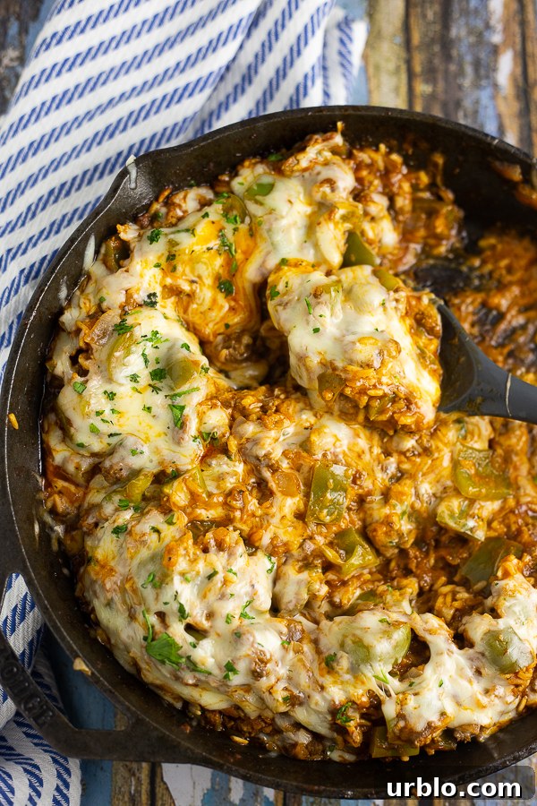 Unstuffed peppers covered in melted mozzarella in a cast iron skillet with a spoon in the middle