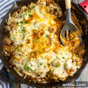Unstuffed peppers covered in melted mozzarella in a cast iron skillet with a spoon in the middle