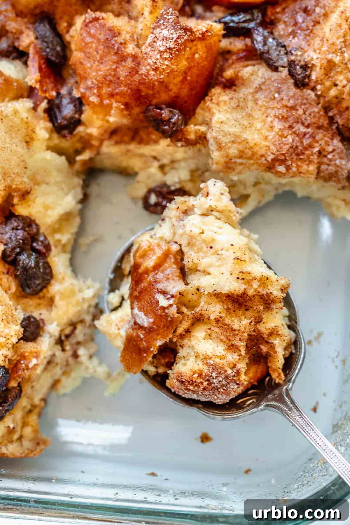 A serving spoon holds a spoonful of cinnamon bread pudding in a casserole dish.