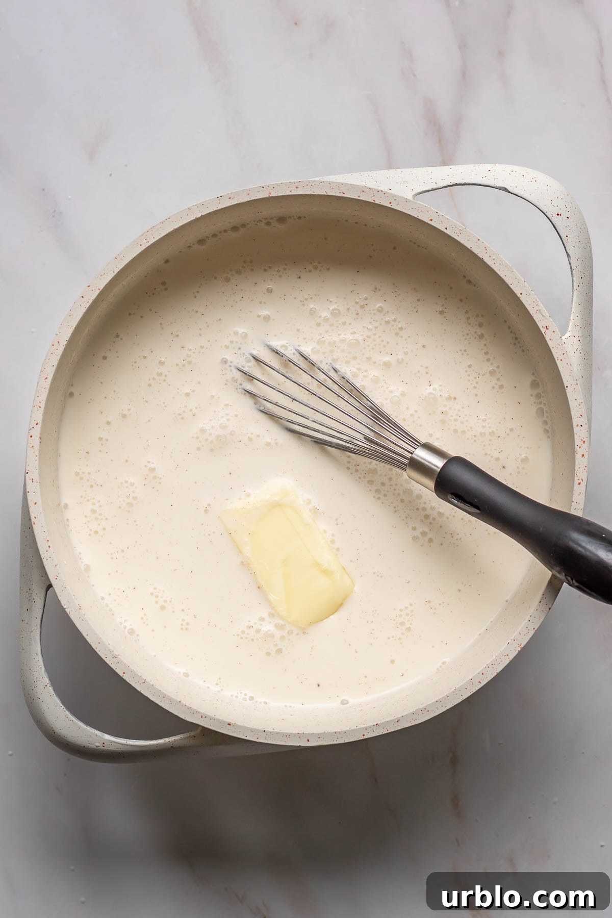 Heavy cream, milk and butter being whisked in a saucepan.