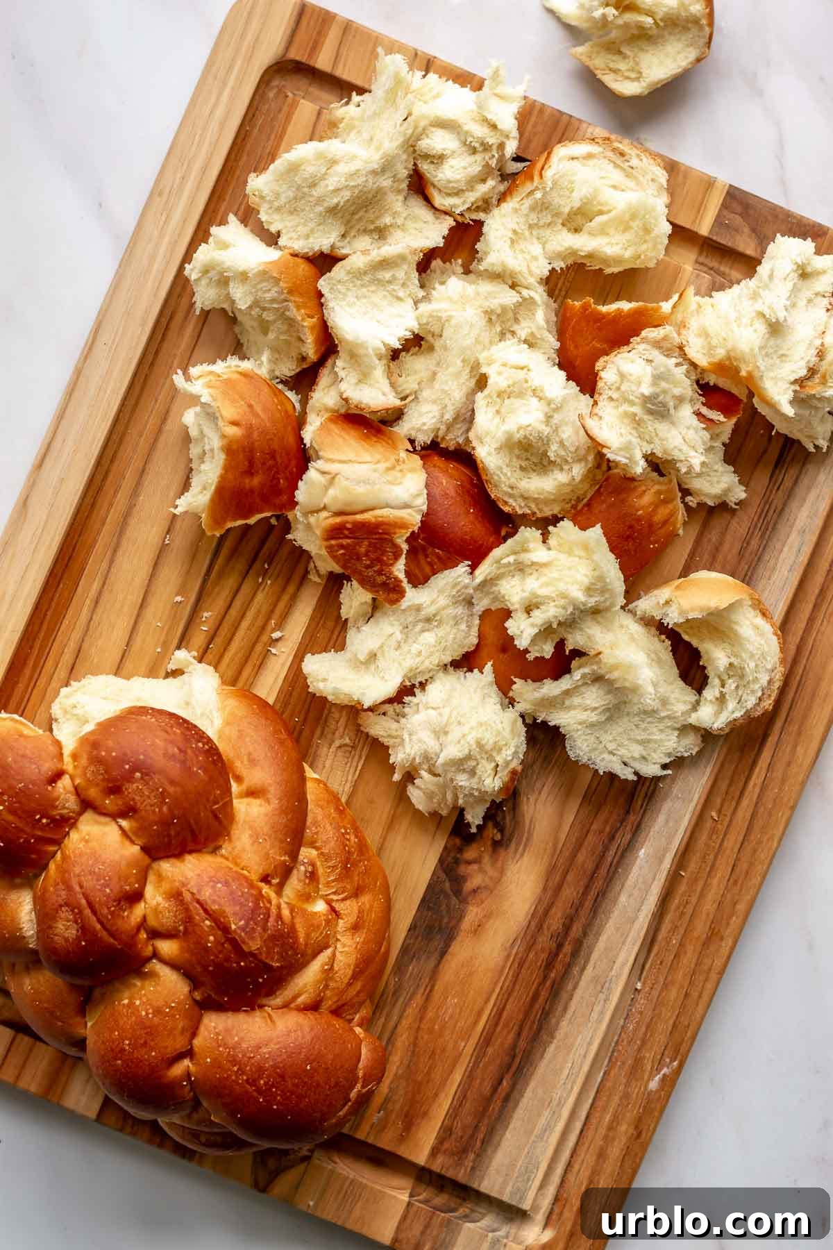 Challah bread ripped apart into pieces on a cutting board.