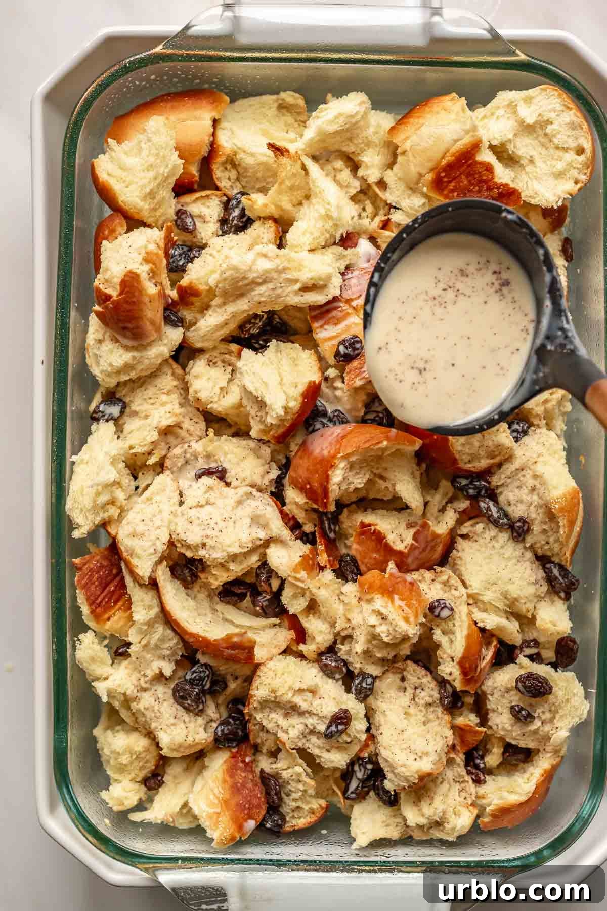 A ladle spoons cinnamon custard over challah pieces.