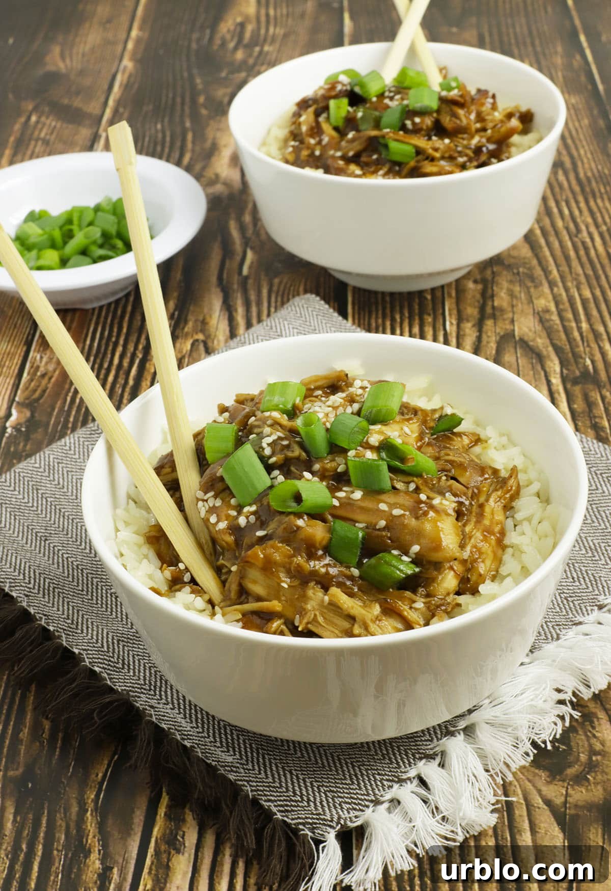 Side view of two white bowls with rice and chicken and chopsticks sticking out.
