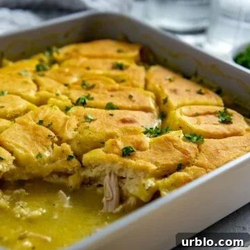 Baked chicken cobbler in a square casserole dish with one serving removed.