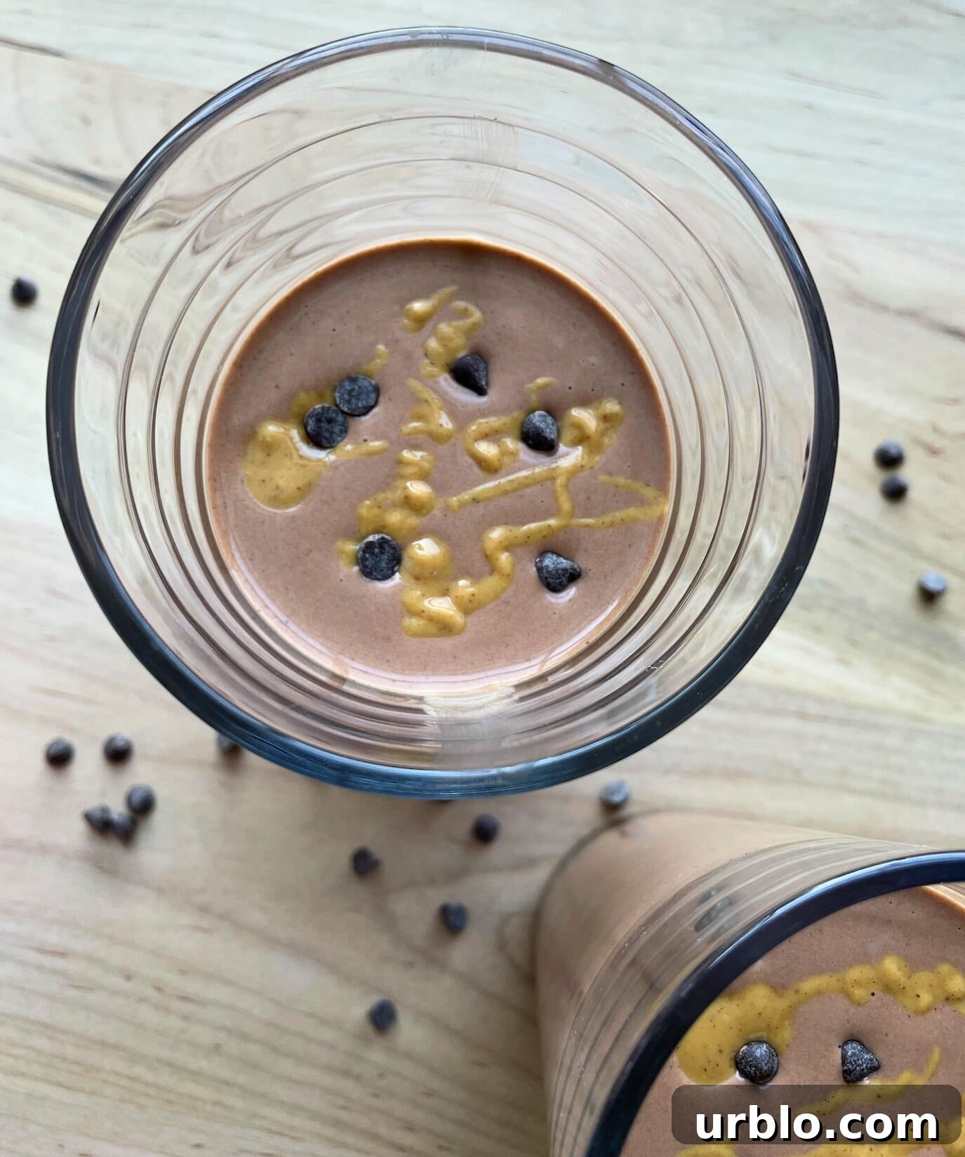A chocolate peanut butter banana smoothie with peanut butter drizzled over the top and chocolate chips sprinkled around.