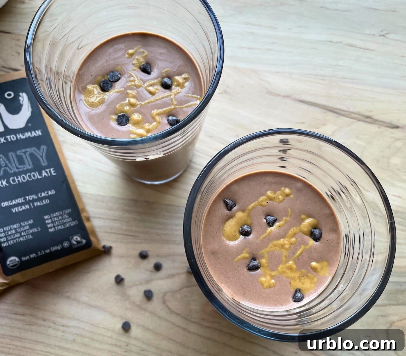Two chocolate peanut butter banana smoothies with peanut butter drizzled over the top and chocolate chips sprinkled around.