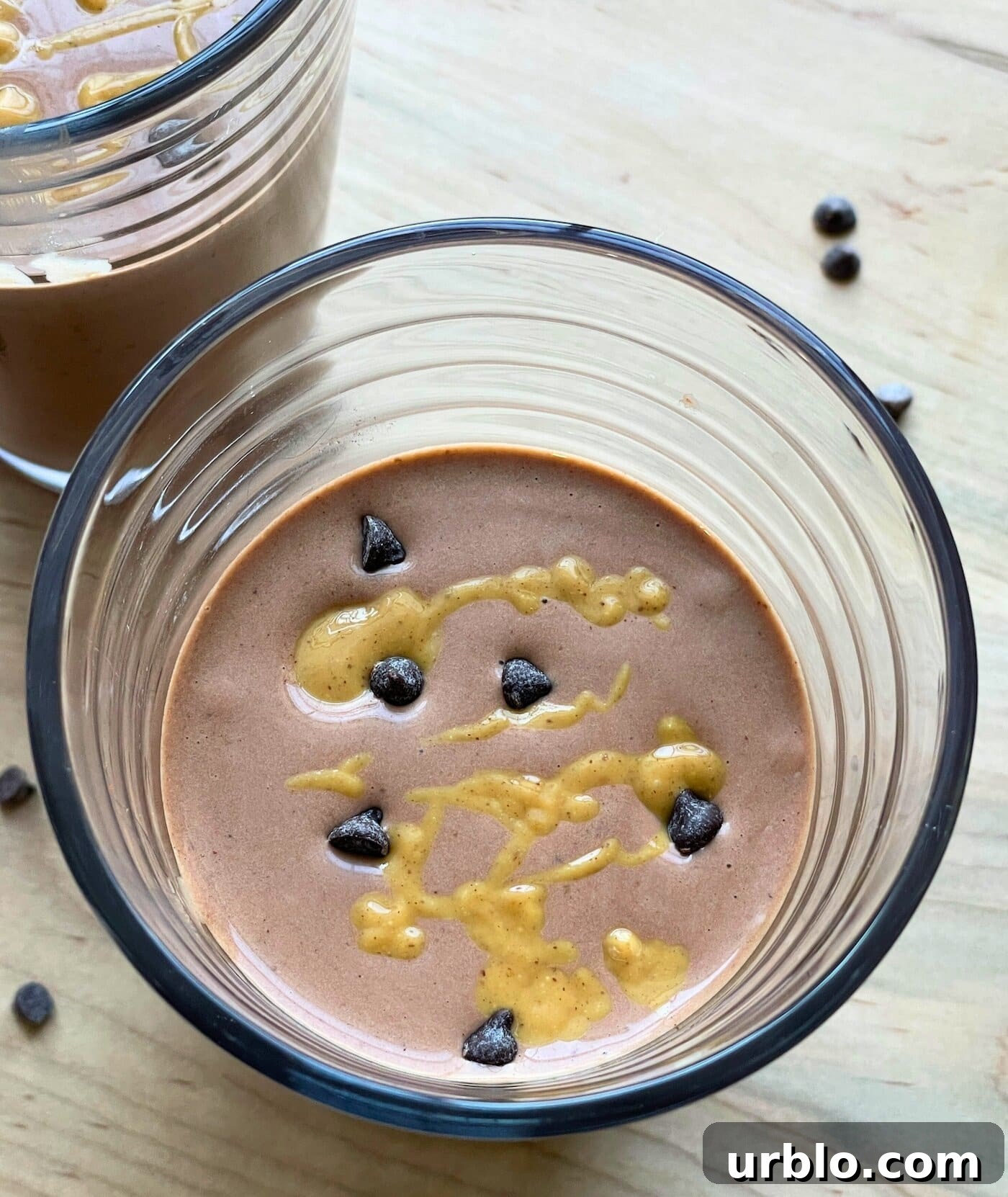 A chocolate peanut butter banana smoothie with peanut butter drizzled over the top and chocolate chips sprinkled around.
