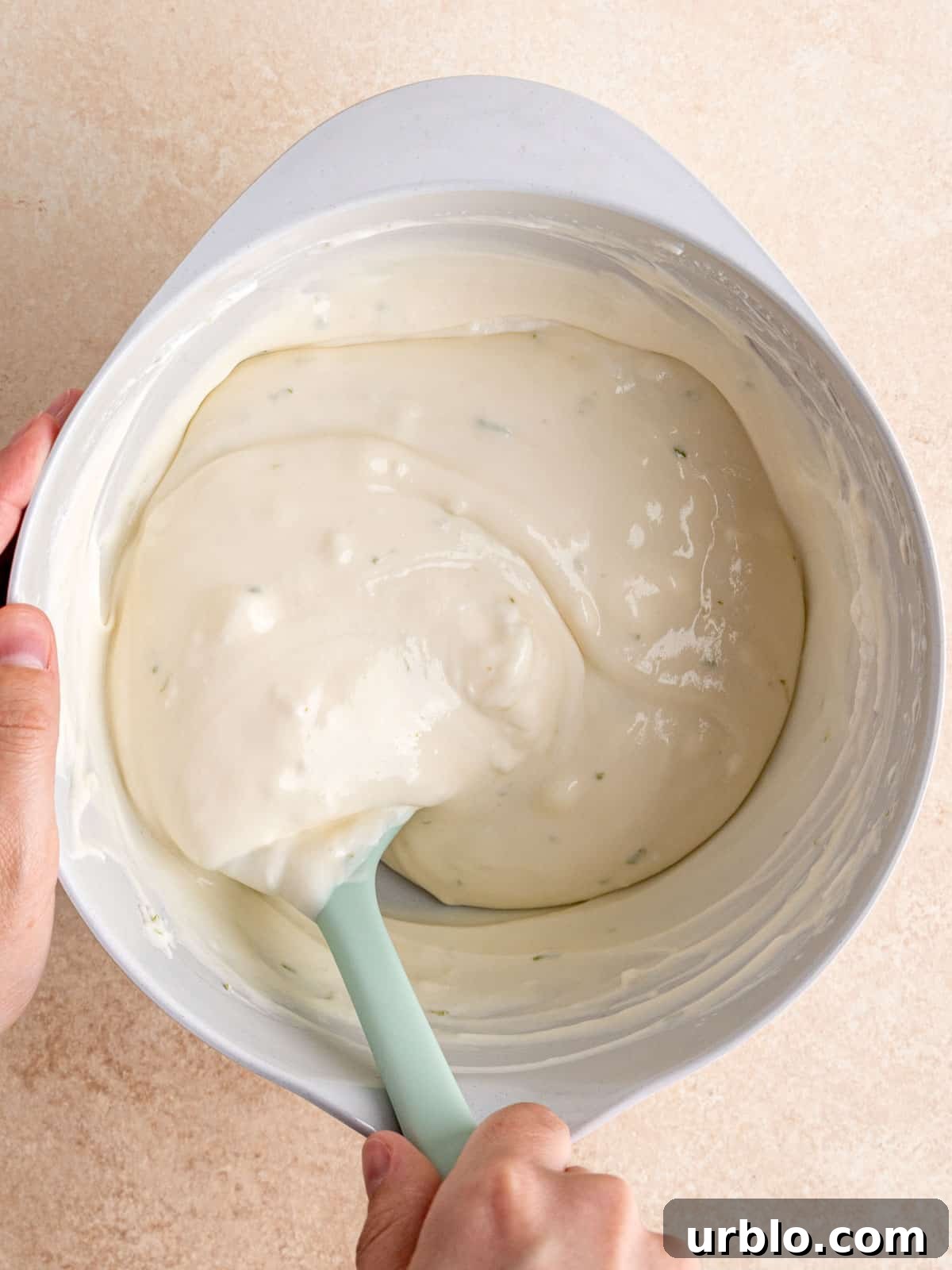 Folding whipped cream into key lime pie cheesecake mixture in a bowl.