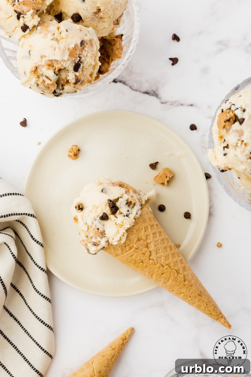 a sugar cone topped with a scoop of cookie dough ice cream, set down on a round white plate.