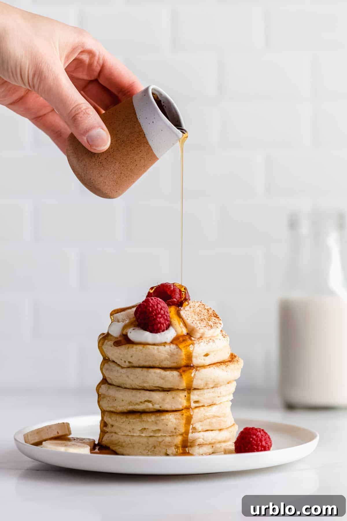 a hand pouring maple syrup onto a stack of vegan oatmeal pancakes
