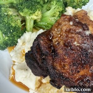 A close-up of a plate with Easy Weeknight Juicy Chicken Thighs, mashed potatoes, brown gravy, and steamed broccoli. The chicken is crispy and golden-brown, paired perfectly with creamy mashed potatoes and fresh broccoli.