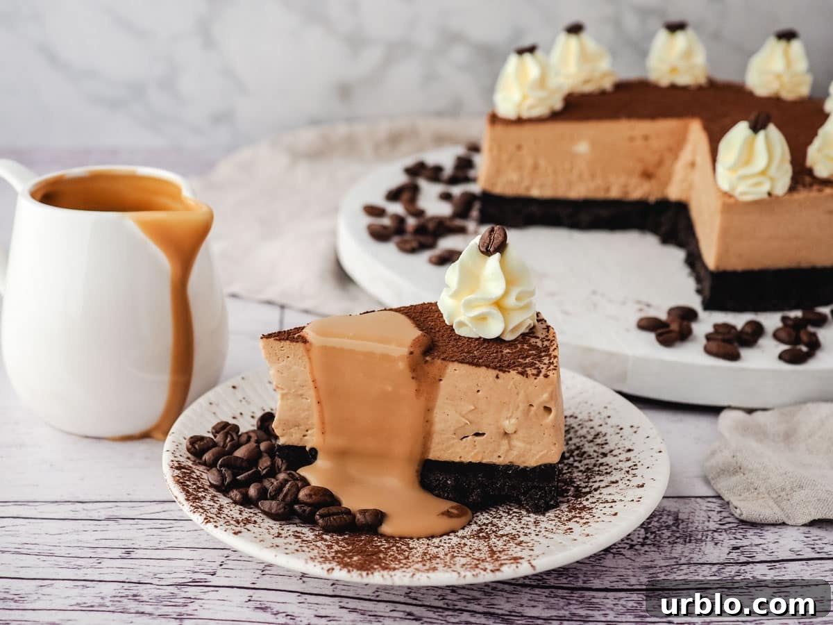 A slice of coffee cheesecake with coffee sauce drizzled on it, with jug of coffee sauce and rest of cheesecake in the background.