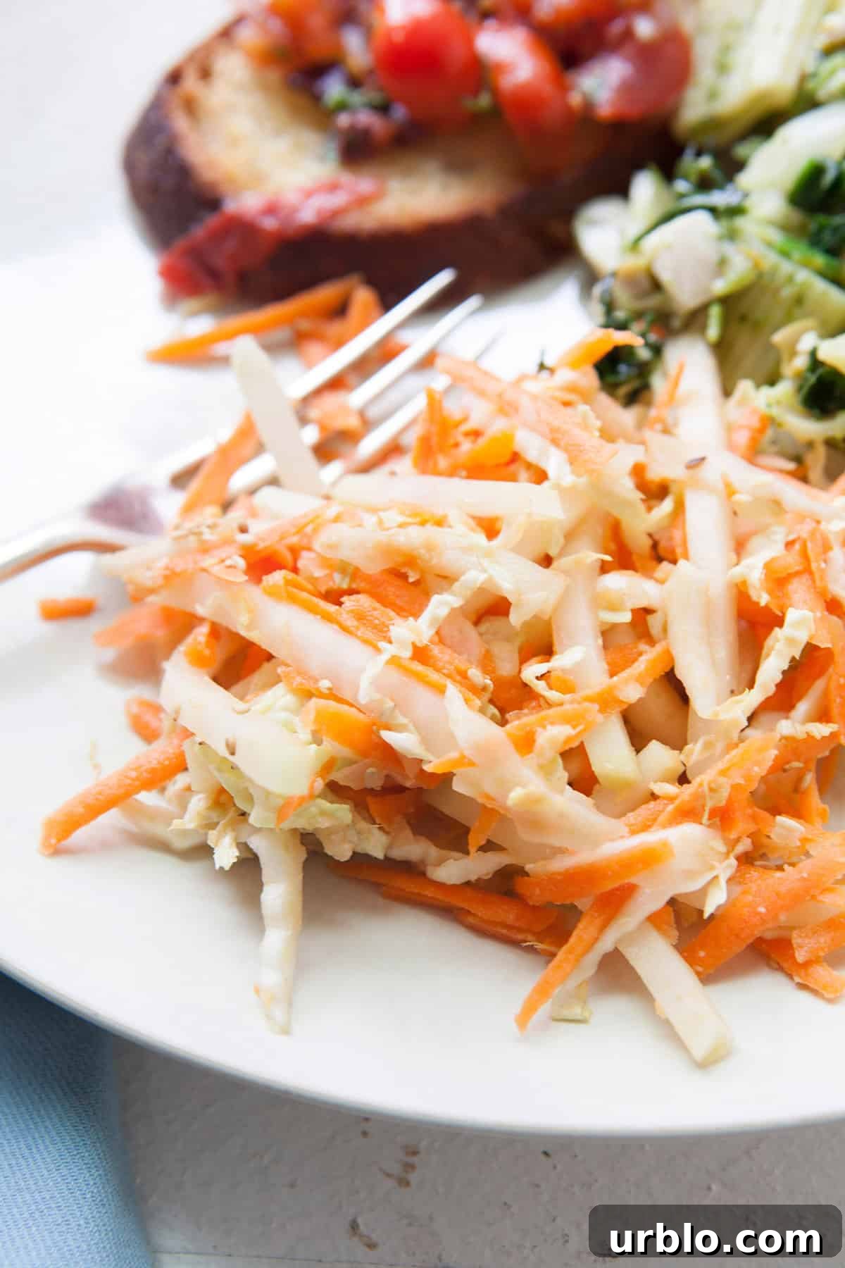 Carrot, Cabbage, and Kohlrabi Slaw with Miso Dressing on white plate with blue napkin.