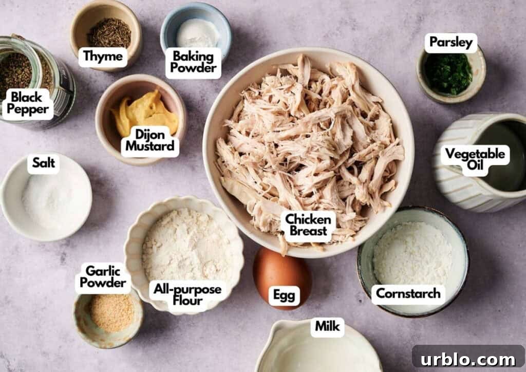 Overhead view of labeled ingredients in bowls for chicken fritters, including shredded chicken breast, egg, milk, flour, cornstarch, garlic powder, salt, black pepper, thyme, baking powder, dijon mustard, parsley, and vegetable oil.