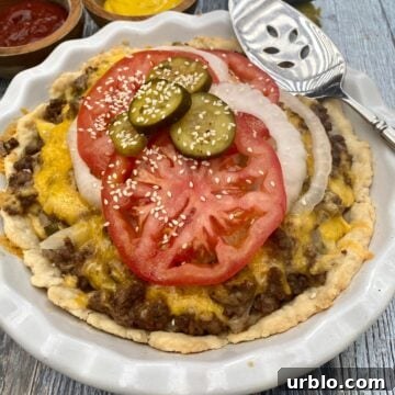 Cheeseburger pie in a pie plate with tomato and onion and sliced pickle on wooden planks