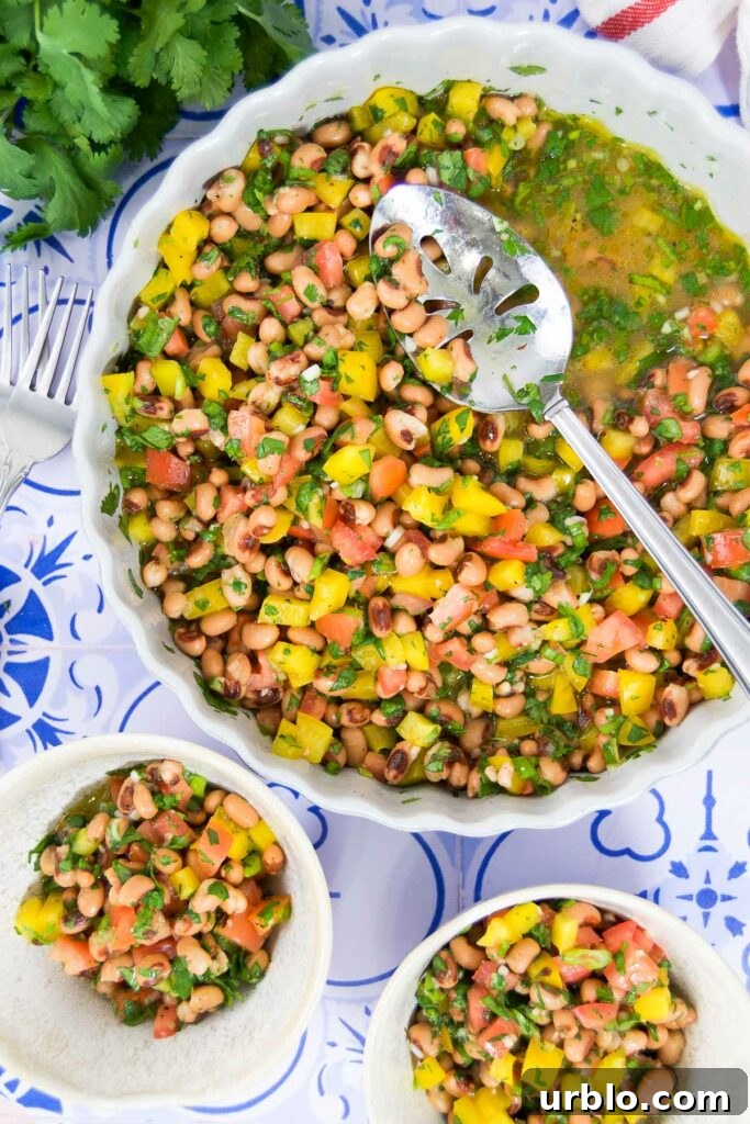 Close up of a serving bowl of black eyed pea salad recipe next two two serving bowls on a tile table