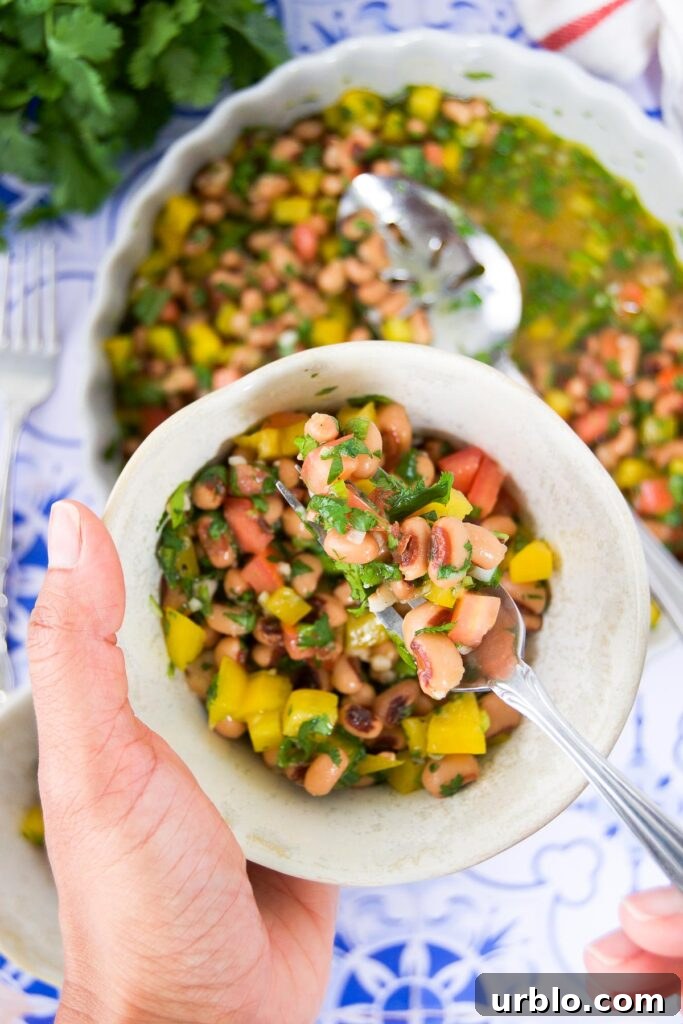 A woman holds a serving bowl of black eyed pea salad along with a fork