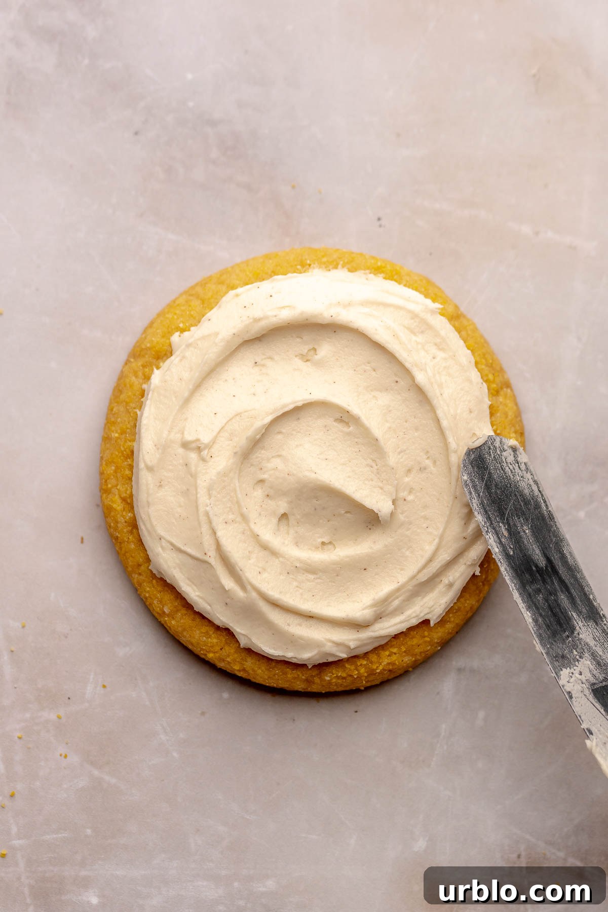 A spatula spreads honey buttercream onto a cornbread cookie.