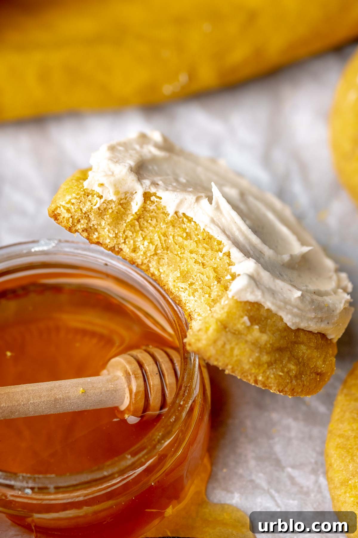 A frosted cornbread cookie with a bite removed leaning on a bowl of honey.