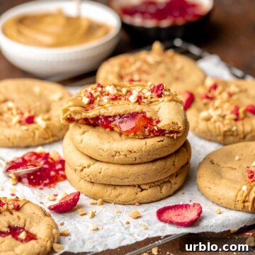 A stack of peanut butter and jelly cookies. The top cookie is broken open.