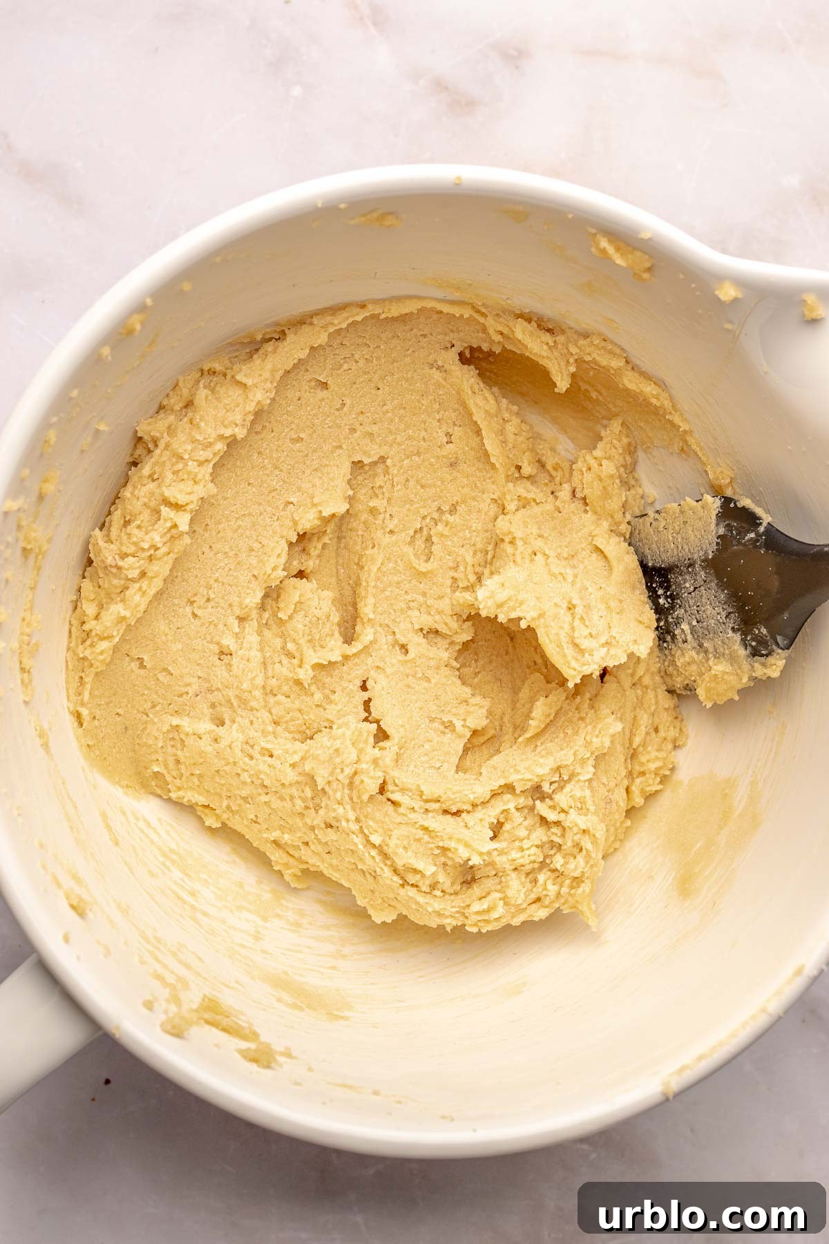 Creamed butter and sugar in a bowl with a rubber spatula.