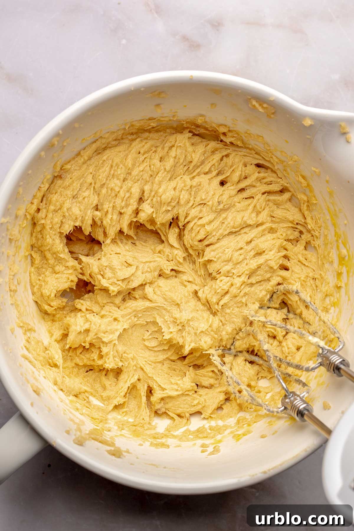 A hand mixer beats wet ingredients in a bowl.