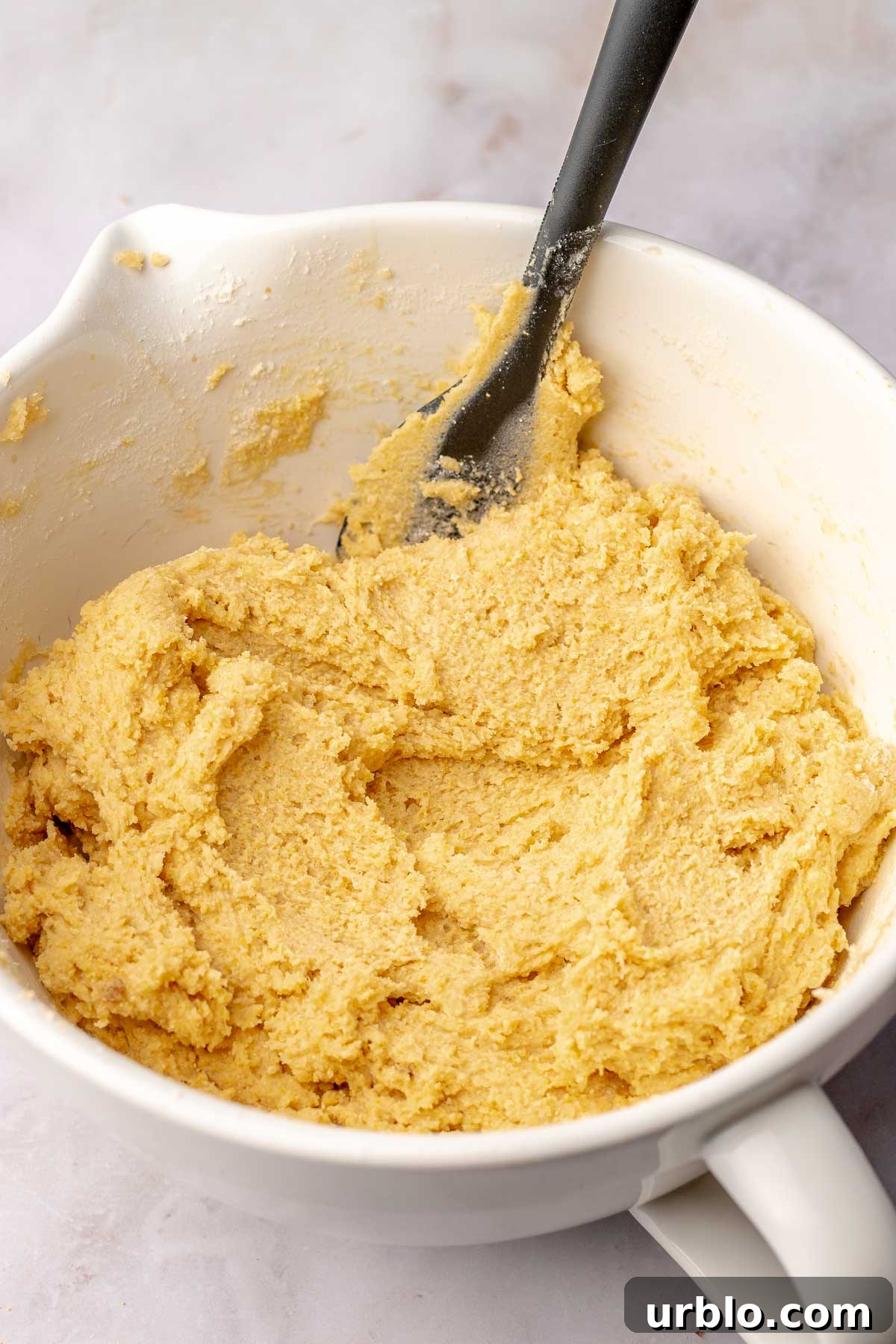 Cornbread cookie dough in a bowl with a rubber spatula.