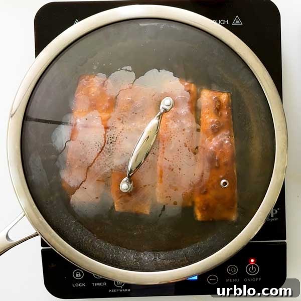 Salmon cooking in a frying pan with a lid.