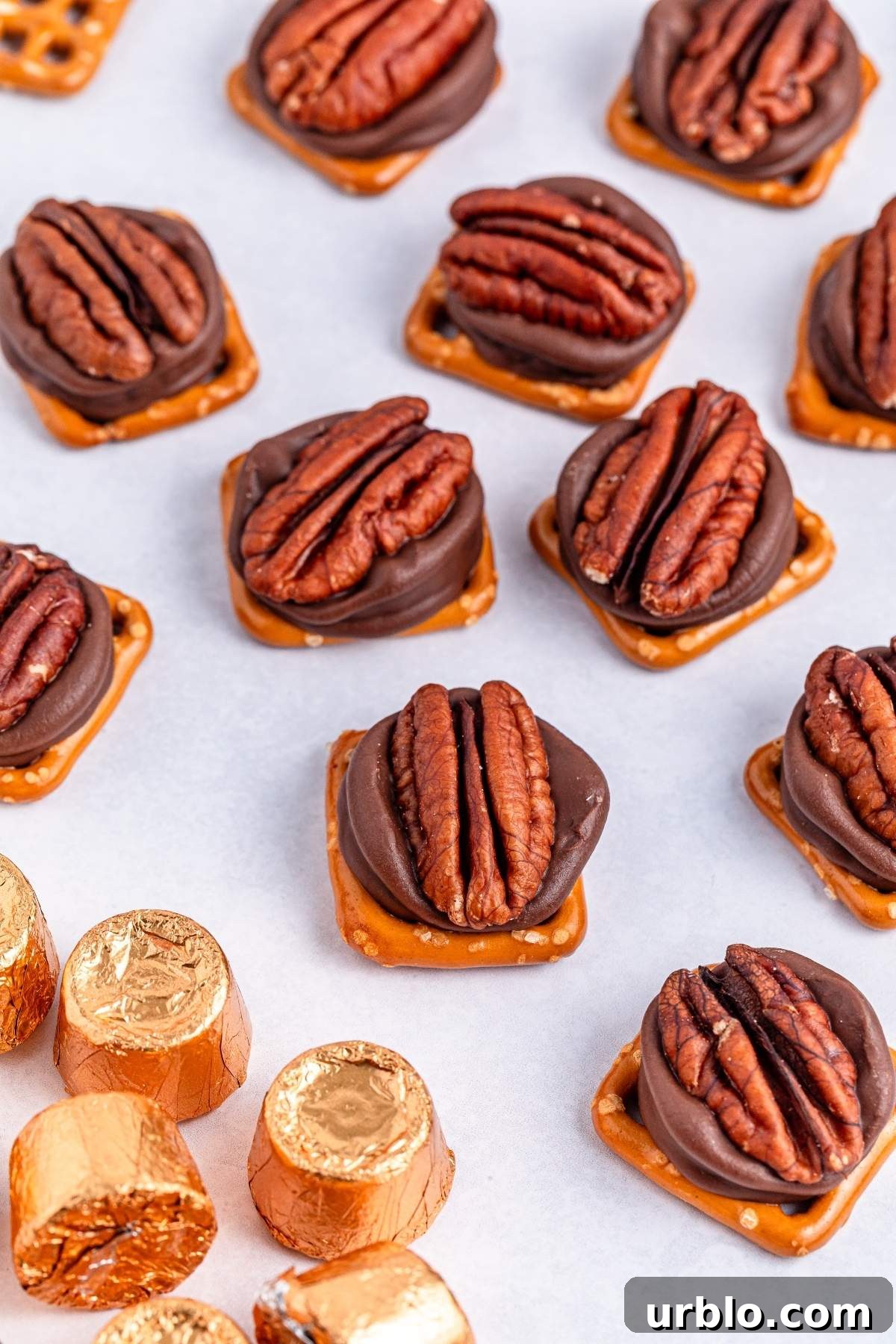 3-ingredient pretzel Rolo turtle candy bites on a white surface, with gold-wrapped chocolates nearby.