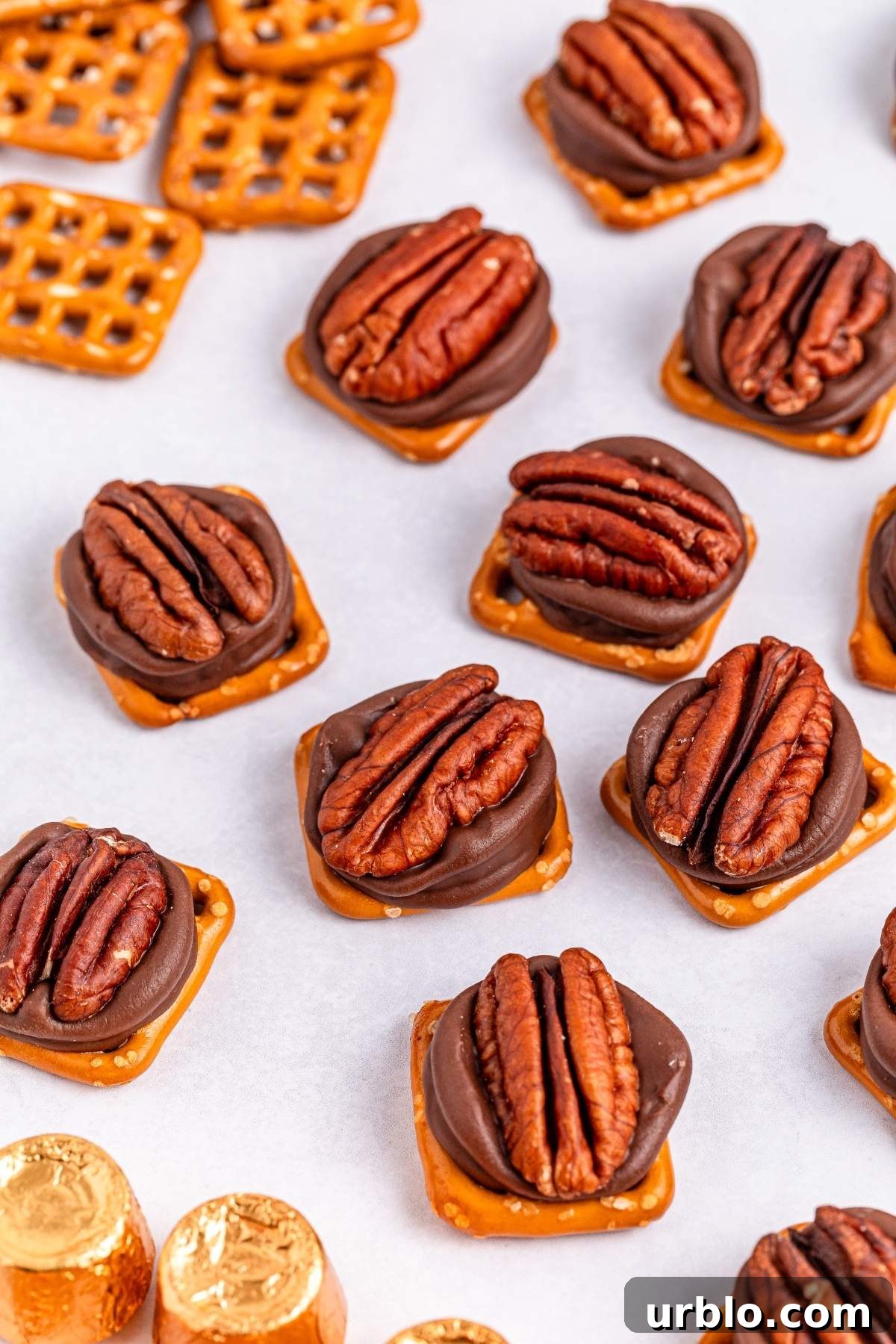 Pretzel turtle bites feature pretzel squares topped with melted chocolate, pecan halves, and caramel candies, all elegantly arranged on a white surface.