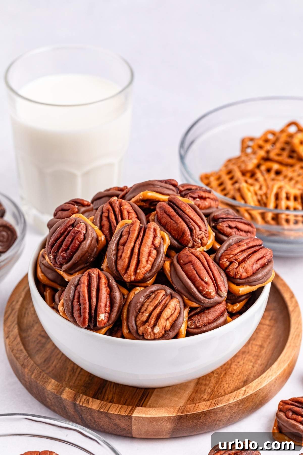 A bowl of 3-ingredient pretzel Rolo turtle bites, a glass of milk, and additional bowls of pretzel turtle bites in the background.