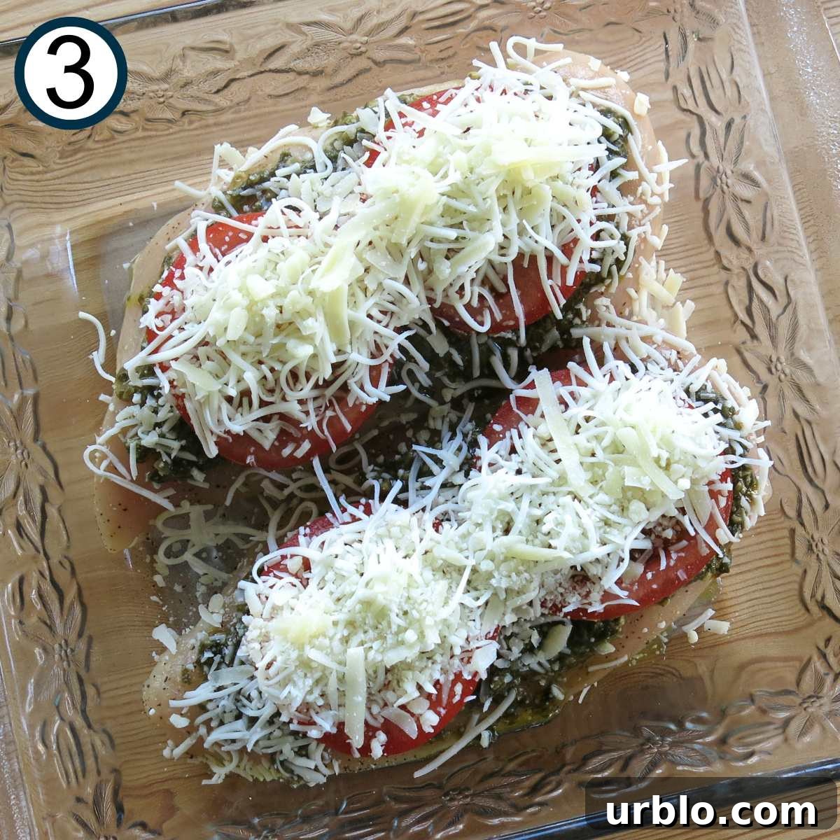 Crispy Baked Pesto Chicken Breast with Parmesan Crust 5 Shredded mozzarella cheese layered on top of two chicken breasts layered with pesto and tomatoes in a glass baking dish.