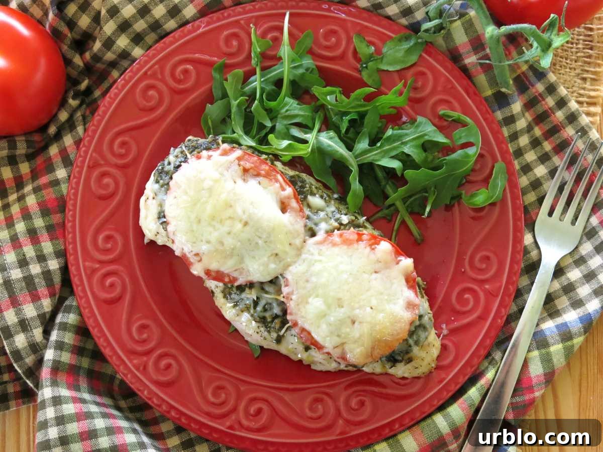 Crispy Baked Pesto Chicken Breast with Parmesan Crust 7 Baked chicken breast topped with pesto, sliced tomatoes, mozzarella, and Parmesan cheese on a red plate with a little arugula.