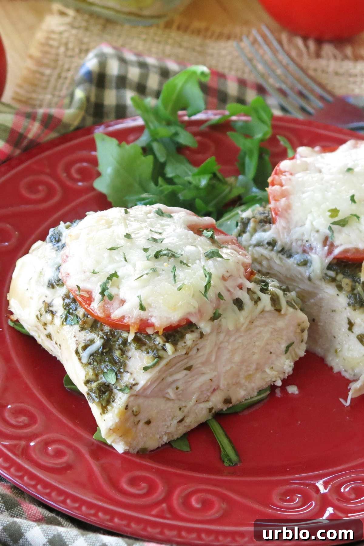 Crispy Baked Pesto Chicken Breast with Parmesan Crust 8 Close-up of juicy center of baked pesto chicken breast on a red plate with arugula behind it.